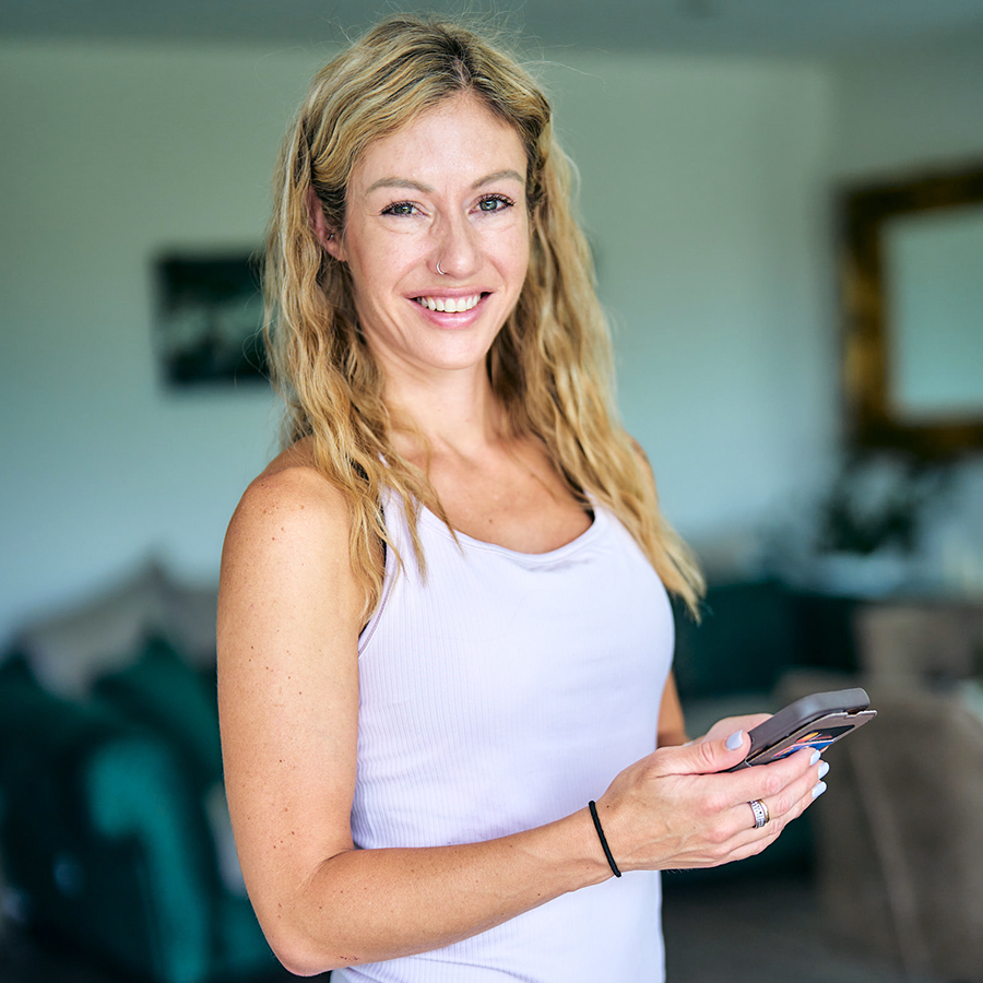 Jacqueline Moser – Personal Trainerin aus Thun erreichbar per WhatsApp Jacqueline Moser, Personal Trainerin für die Region Thun und Umgebung, lächelt mit Smartphone in der Hand und ist jederzeit per WhatsApp erreichbar